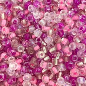 K&ouml;nnte beinhalten: Nahaufnahme einer Vielzahl von Perlen in den Farben Rosa, Lila und Klar. Die Perlen sind irisierend und haben eine leicht durchscheinende Optik.