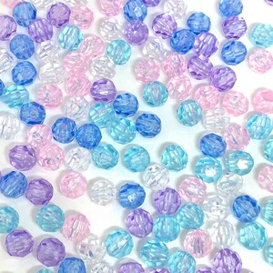May include: A collection of faceted plastic beads in various shades of blue, pink, and clear. The beads are scattered on a white background.