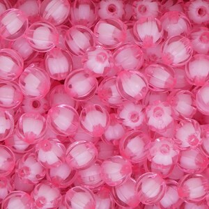 May include: A close-up shot of a pile of translucent pink beads. The beads have a ribbed design and a white core. Some beads have a flower-like shape. The beads are scattered, filling the frame.