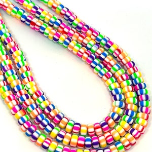 Könnte beinhalten: Eine Strähne bunter, gestreifter Perlen. Die Perlen sind weiß mit abwechselnden Streifen in Pink, Orange, Gelb, Grün, Blau und Lila.