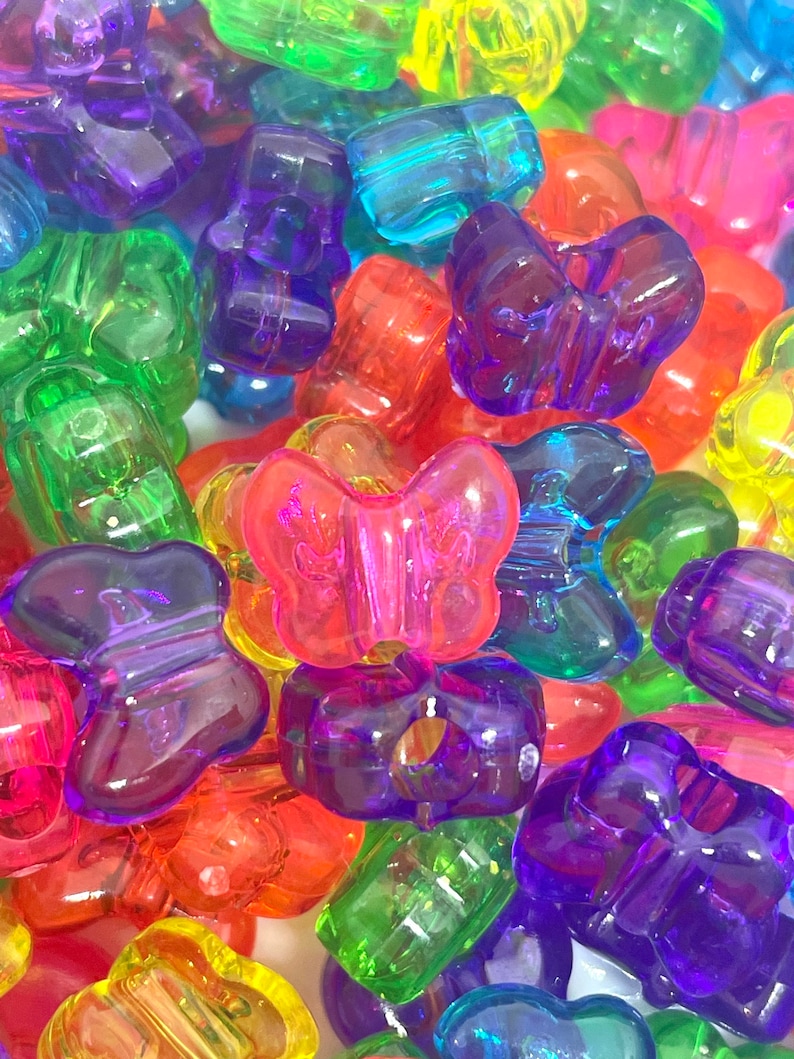 May include: A collection of colorful plastic butterfly beads. The beads are translucent and have a variety of colors, including red, orange, yellow, green, blue, purple, and pink.