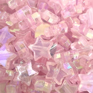 May include: A close-up of a pile of iridescent pink star-shaped beads. The beads are made of glass and have a shiny, reflective surface.
