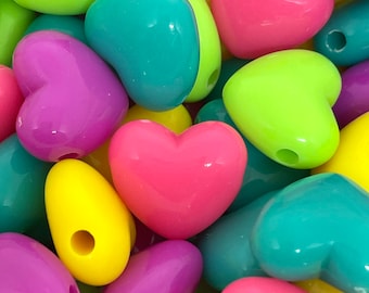 May include: A close-up of a pile of colorful heart-shaped beads. The beads are made of plastic and come in a variety of colors, including pink, yellow, green, blue, and purple.