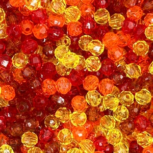 May include: A close-up shot of a pile of faceted beads in shades of red, orange, and yellow. The beads are round and have a shiny, transparent appearance. The colors blend together, creating a warm and vibrant effect. These beads are suitable for jewelry making and crafts.
