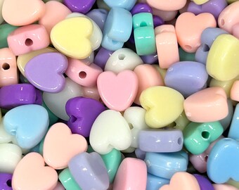 May include: A large pile of pastel-colored heart-shaped beads. The beads are made of plastic and have a smooth, glossy finish. The colors include pink, purple, blue, yellow, and green.