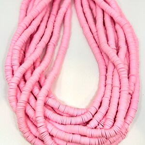 May include: A large strand of pink polymer clay beads. The beads are flat and round, and they are strung together in a long, continuous strand.
