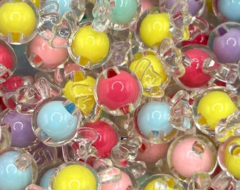 May include: A close-up of a pile of colorful plastic beads with clear plastic bows. The beads are in various colors, including pink, yellow, blue, and purple.