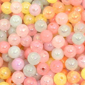 May include: A close-up of a large assortment of iridescent pastel-colored beads. The beads are round and have a smooth, glossy finish. They are perfect for crafting jewelry, making garlands, or adding a touch of whimsy to any project.
