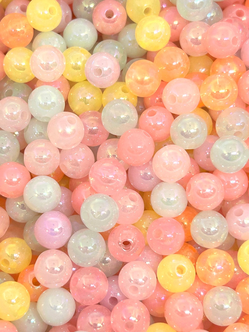 May include: A close-up of a large assortment of iridescent pastel-colored beads. The beads are round and have a smooth, glossy finish. They are perfect for crafting jewelry, making garlands, or adding a touch of whimsy to any project.