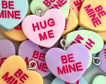 May include: Assortment of colorful heart-shaped candy charms with various Valentine's Day messages, including "Be Mine", "Hug Me", and "Love You".