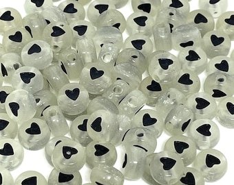 May include: A pile of white, translucent round beads with black heart designs.