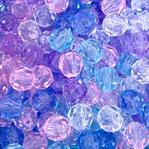May include: A close-up of a pile of colorful faceted beads in shades of blue, purple, and pink. The beads are made of clear plastic and have a shiny finish.