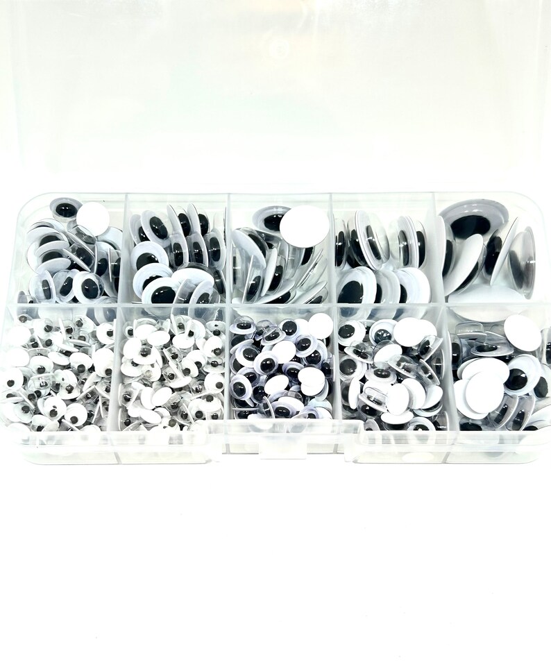 May include: A clear plastic storage box filled with various sizes of googly eyes. The googly eyes are black and white and come in a variety of sizes.