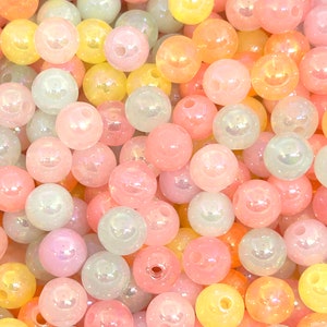 May include: A collection of iridescent pastel-colored beads in shades of pink, yellow, and green. The beads are round and have a smooth, glossy finish.