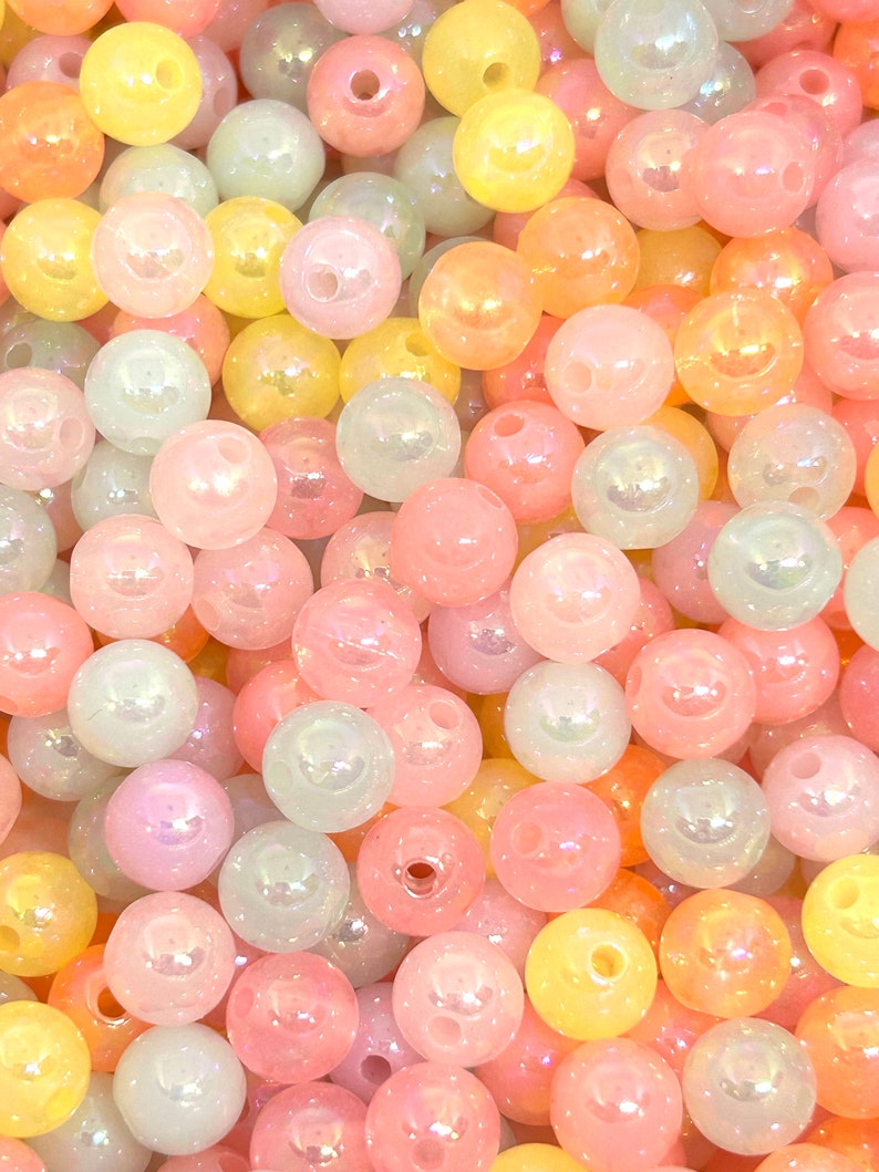 May include: A collection of iridescent pastel-colored beads in shades of pink, yellow, and green. The beads are round and have a smooth, glossy finish.