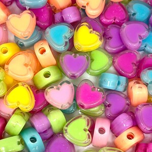 May include: A close-up of a variety of colorful heart-shaped beads. The beads are made of clear plastic with a solid color heart inside. The colors include pink, yellow, green, blue, and purple.