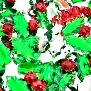 May include: A close-up of a pile of green and red plastic holly leaf charms. The charms are shiny and have a festive look.