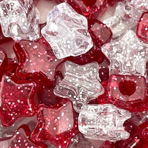May include: A close-up of red and clear star-shaped beads with glitter. The beads are made of plastic and have a shiny finish.