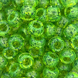 May include: A close-up of a pile of green and black speckled plastic beads. The beads are round with a hole in the center.