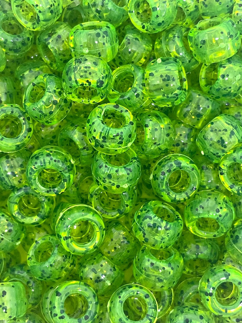May include: A close-up of a pile of green and black speckled plastic beads. The beads are round with a hole in the center.