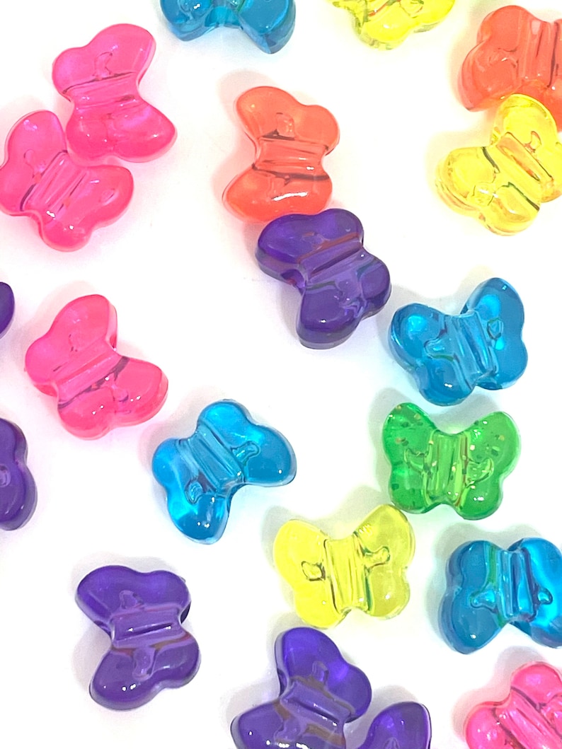 May include: Assortment of colorful plastic butterfly beads. The beads are translucent and come in a variety of colors, including pink, orange, yellow, green, blue, and purple.