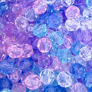 May include: A close-up of a pile of colorful, faceted, plastic beads. The beads are translucent and have a variety of shades of blue, purple, and pink.