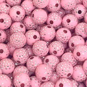 May include: A close-up shot of numerous pink beads with a glossy finish. Each bead is adorned with small, silver-colored embellishments, creating a sparkling effect. The beads have a hole running through the center, suggesting they are for jewelry making or crafts.
