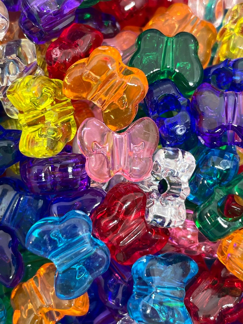 Pu&ograve; includere: Assortimento di perline di plastica a forma di farfalla colorate. Le perline sono trasparenti e disponibili in una variet&agrave; di colori, tra cui rosso, blu, verde, giallo, arancione e viola.