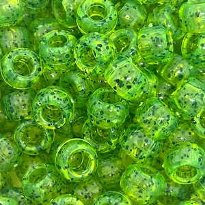 May include: A close-up of a large quantity of lime green and black speckled round beads with a hole in the center. The beads are made of plastic and have a glossy finish.