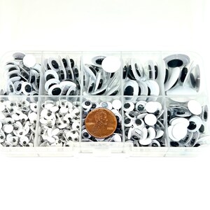 May include: A clear plastic storage box filled with various sizes of black and white googly eyes. The box has eight compartments and a penny is included for size reference.