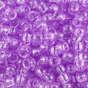 May include: A close-up image of a large quantity of small, translucent purple plastic beads. The beads are round and have a hole in the centre. They are commonly used for making jewellery or crafts.