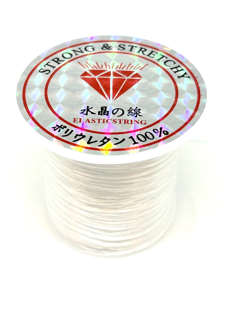Pu&ograve; includere: Filo elastico bianco su una bobina con un'etichetta olografica che recita "Strong & Stretchy" e "Elastricstring 100%".