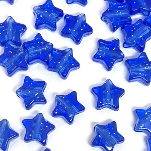 May include: A collection of blue star-shaped glass beads with a sparkly finish. The beads are scattered on a white surface.