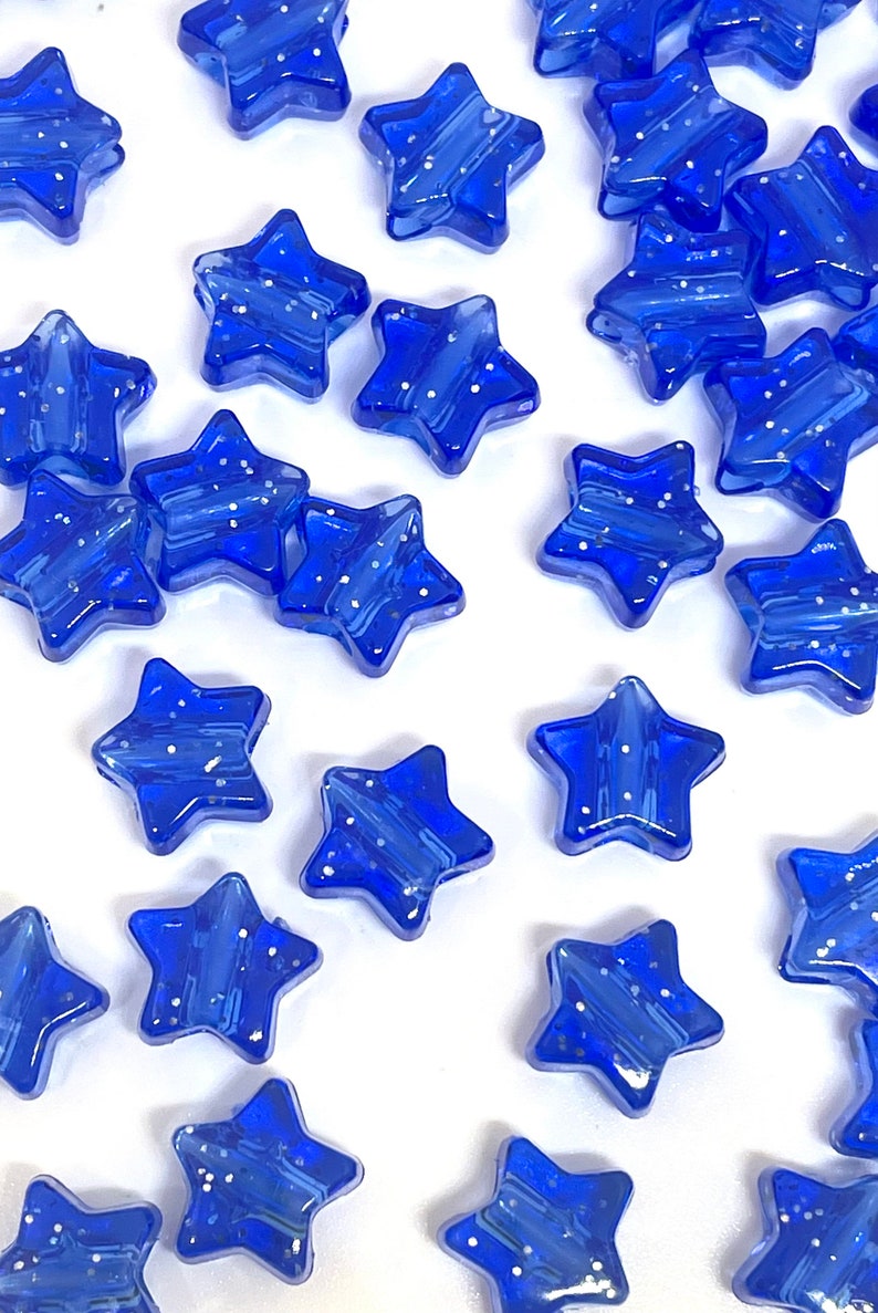 May include: A collection of blue star-shaped glass beads with a sparkly finish. The beads are scattered on a white surface.