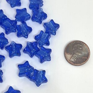 May include: A collection of blue star-shaped beads with white glitter accents. The beads are approximately the size of a US penny.