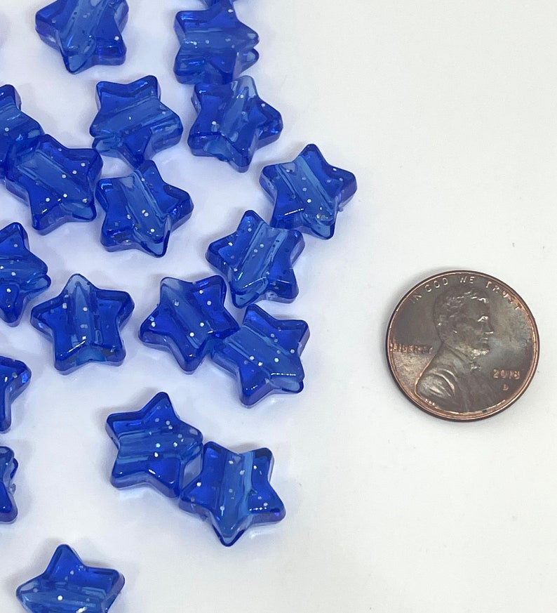 May include: A collection of blue star-shaped beads with white glitter accents. The beads are approximately the size of a US penny.