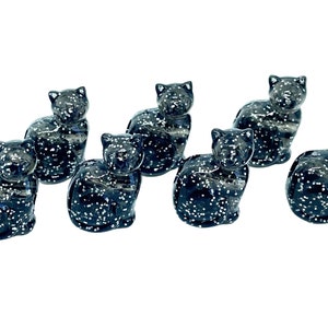 May include: Six black glitter cat figurines. The cats are sitting with their tails curled around their bodies. The glitter is white and sparkles.