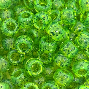 May include: A close-up of a pile of lime green and black speckled plastic beads. The beads are round with a hole in the center.