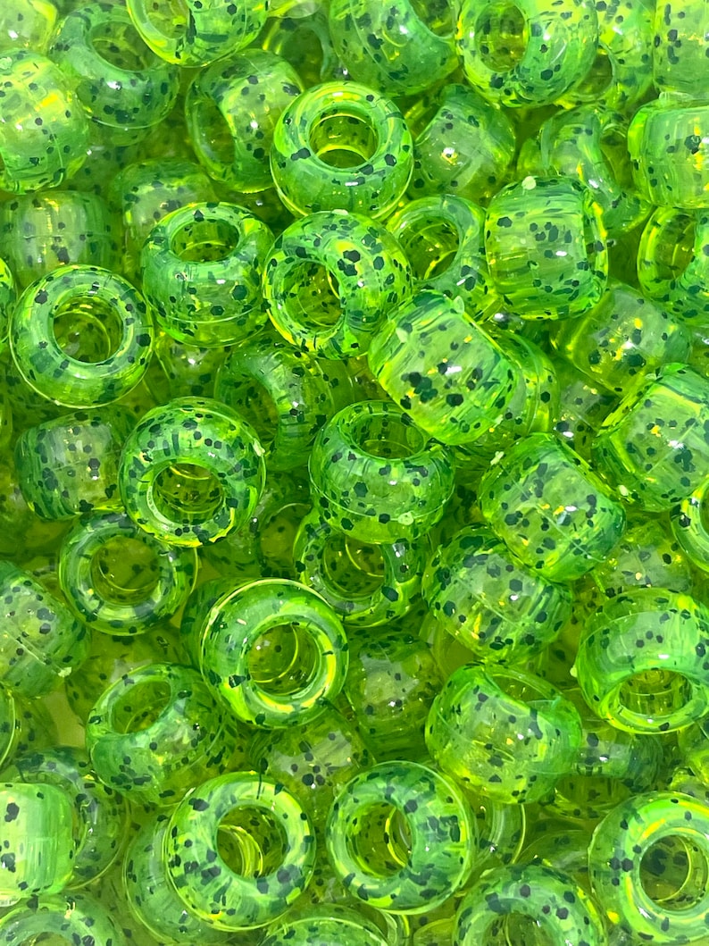 May include: A close-up of a pile of lime green and black speckled plastic beads. The beads are round with a hole in the center.