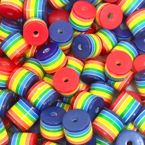 May include: A close-up of a pile of colourful rainbow striped beads. The beads are made of plastic and have a hole in the centre for stringing. The beads are a mix of red, orange, yellow, green, blue, indigo, and violet.
