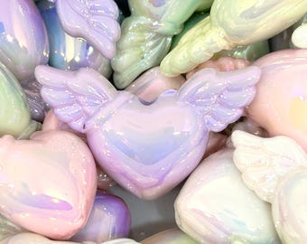 May include: A close-up of iridescent pastel pink, purple, and green heart-shaped beads with wings. The beads are made of glass and have a smooth, shiny finish.