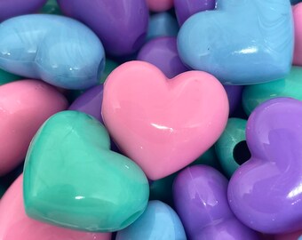 May include: A collection of heart-shaped beads in various pastel colors, including pink, purple, blue, and green. The beads are made of plastic and have a glossy finish.