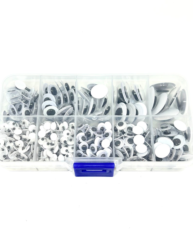 May include: A clear plastic storage box with a blue latch, containing a variety of googly eyes in different sizes. The googly eyes are white with black pupils and are arranged in rows within the box.
