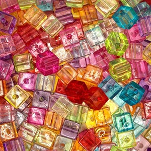 May include: A vibrant assortment of colorful, translucent cube beads. The beads are in various shades of pink, red, orange, yellow, green, blue, and purple. Each cube has a hole running through the center, suggesting they are for jewelry making or crafts.