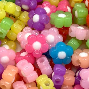 May include: A collection of colorful plastic flower-shaped beads with a white center. The beads are in various shades of pink, purple, blue, green, yellow, and orange.
