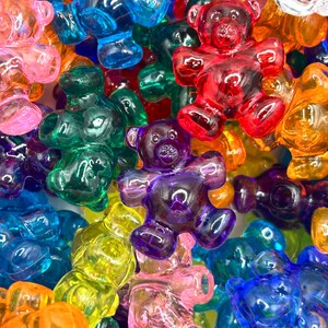 May include: A close-up shot of a collection of colorful gummy bear candies. The bears are in various colors, including red, blue, green, yellow, orange, purple, and pink. The translucent bears are in a variety of poses.