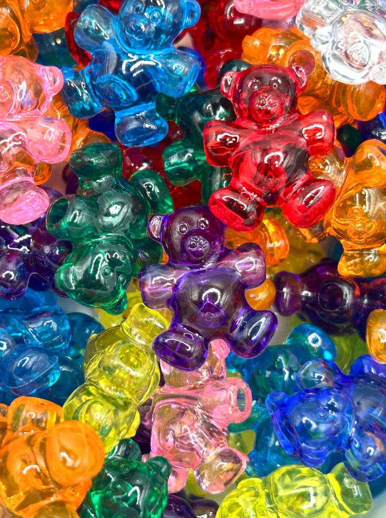 May include: A close-up shot of a collection of colorful gummy bear candies. The bears are in various colors, including red, blue, green, yellow, orange, purple, and pink. The translucent bears are in a variety of poses.