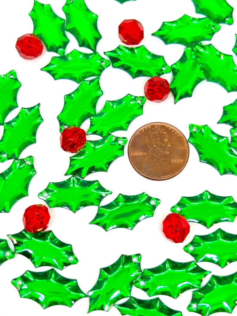 May include: A scattering of green holly leaves with red berry accents. The leaves are shiny and have a slightly iridescent finish. The berries are small and round.