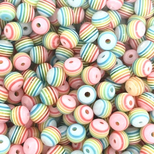 May include: A large pile of colorful striped round beads. The beads are made of plastic and have a glossy finish. The beads are in a variety of colors, including pink, blue, green, yellow, and orange.