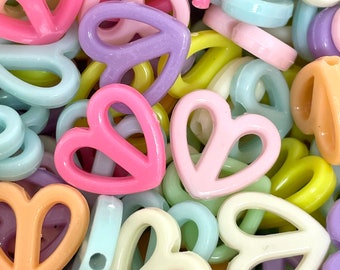 May include: A collection of pastel-colored plastic heart-shaped beads with a hole in the center. The beads are in various shades of pink, yellow, blue, and purple.